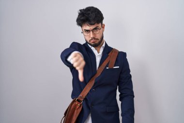 Hispanic man with beard wearing business clothes looking unhappy and angry showing rejection and negative with thumbs down gesture. bad expression. 
