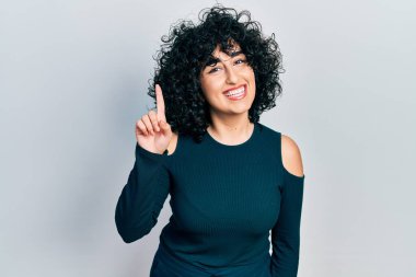 Orta Doğulu genç bir kadın bir fikir veya soruyla gülümsüyor ve mutlu bir yüzle işaret ediyor. 