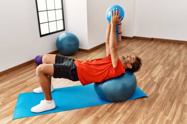 Genç İspanyol gülen adam spor merkezinde formda top kullanarak kendine güvenen bir antrenman yapıyor.