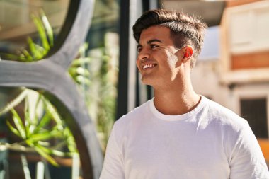 Young hispanic man smiling confident looking to the side at street
