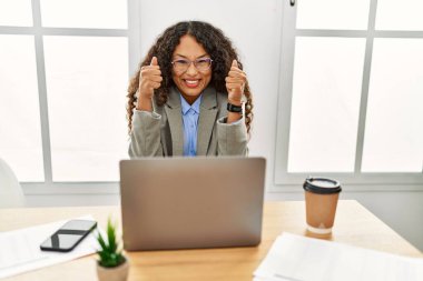 Güzel İspanyol iş kadını ofisinde oturmuş laptopuyla çalışıyor. Başarı için heyecanlı kolları havada ve gözleri kapalı zaferi kutlarken gülümsüyor. Kazanan konsept. 