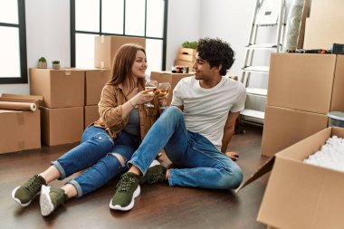 Genç çift yeni evinde kadeh kaldırırken mutlu bir şekilde gülümsüyor..