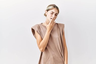 İzole edilmiş arka planda duran genç sarışın kadın elleriyle ağzını kapatmaktan sıkılmış. Huzursuz ve uykulu.. 