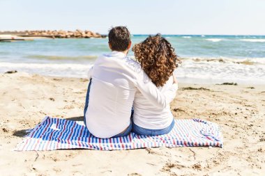 Orta yaşlı İspanyol çift arka planda havluyla kumsalda sarılıyorlar..