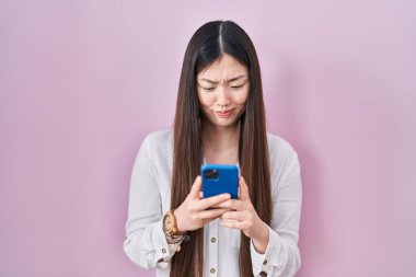 Çinli genç bir kadın akıllı telefon kullanarak şüpheci ve gergin mesajlar yazıyor, sorun yüzünden surat asıyor. negatif kişi. 