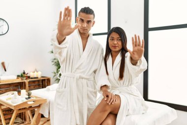 Havlu giymiş genç Latin bir çift güzellik merkezinde el ele şarkı söylemeyi kesiyor. Yüzünde olumsuz ve ciddi bir jest olan uyarı ifadesi. 