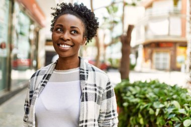 Genç Afrikalı Amerikalı kız gülümseyerek şehirde mutlu mesut duruyor..