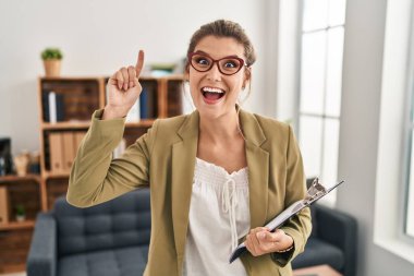 Muayenehanede çalışan genç bir kadın şaşırmış, şaşırmış ve parmaklarıyla işaret ediyor ve kollarını kaldırıyordu.. 