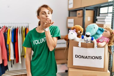 Beautiful caucasian woman wearing volunteer t shirt at donations stand looking at the camera blowing a kiss with hand on air being lovely and sexy. love expression. 