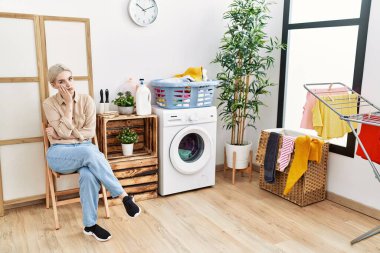 Young caucasian woman boring waiting for washing machine at laundry room