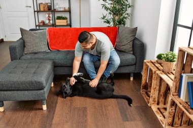 Genç İspanyol gülümseyen adam evde köpekle oynarken mutlu oluyor..