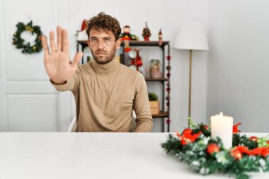 Noel süslemesi masasında oturan sakallı yakışıklı genç adam avucunun içi gibi şarkı söylemeyi kesiyor. Yüzünde olumsuz ve ciddi bir jest olan uyarı ifadesi. 