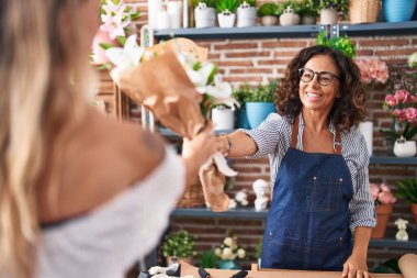 Middle age woman florist giving bouquet of flowers to client at flower shop