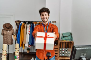 Genç İspanyol esnaf gülümseyerek giyim mağazasında hediyesini tutuyor..
