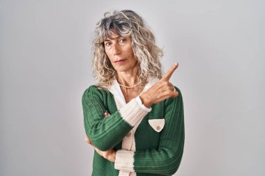 Beyaz arka planda duran orta yaşlı bir kadın, elini yana uzatarak reklamını yapıyor, ciddi ve sakin bir yüz ifadesi var. 