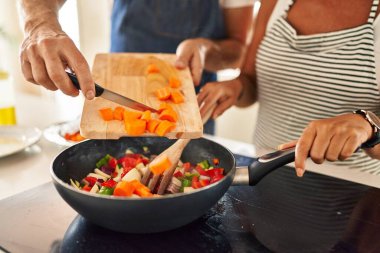 Orta yaşlı İspanyol çift mutfakta tavaya yemek döküyor.