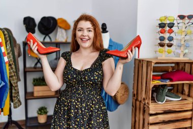 Genç kızıl saçlı kadın, yüksek topuklu ayakkabı mağazasından alışveriş yapıyor.