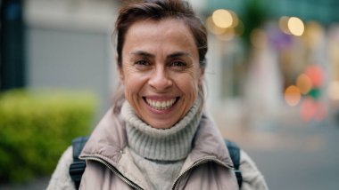 Orta yaşlı İspanyol kadın sokakta kendine güvenerek gülümsüyor.