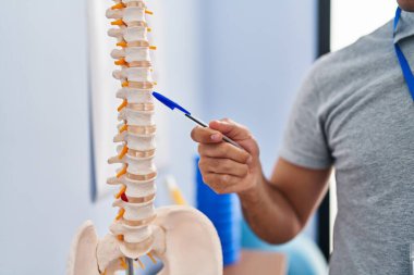 Genç İspanyol fizyoterapist rehabilitasyon kliniğindeki omurgayı işaret ediyor.