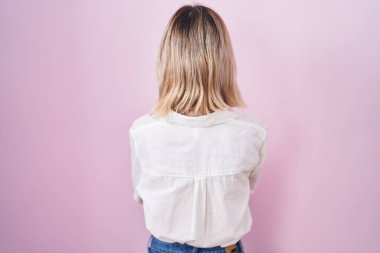 Young beautiful woman standing over pink background standing backwards looking away with crossed arms 
