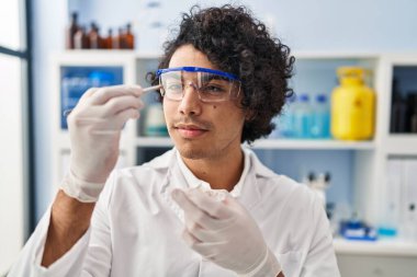 Laboratuvarda elinde cımbızla bilim adamı üniforması giyen genç bir İspanyol.