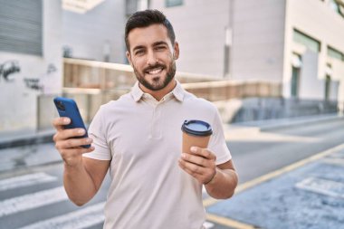 Genç İspanyol adam akıllı telefon kullanıyor, sokakta kahve içiyor.