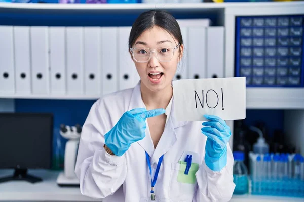 Chinese young woman working at scientist laboratory holding no banner smiling happy pointing with hand and finger