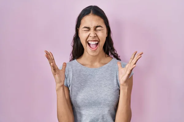 ピンクの背景にカジュアルなTシャツを着た若いブラジル人女性は 腕を上げて興奮して叫んで目を閉じて成功のために狂気と狂気を祝います 勝者のコンセプト — ストック写真