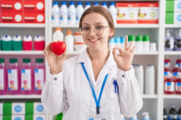 Молодая Кавказская Женщина Работающая Аптеке Держит Красное Сердце Делает Знак — стоковое фото