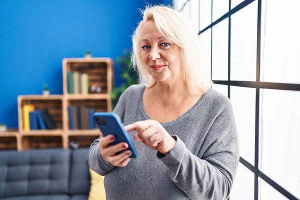 Middle Age Blonde Woman Using Smartphone Standing Home — Foto de Stock