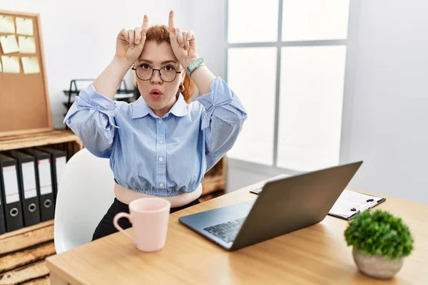 Ofiste Çalışan Genç Kızıl Saçlı Kadın Bilgisayarını Kullanıyor Boynuzlarını Parmağında — Stok fotoğraf
