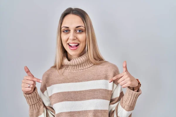 Young blonde woman wearing turtleneck sweater over isolated background looking confident with smile on face, pointing oneself with fingers proud and happy.