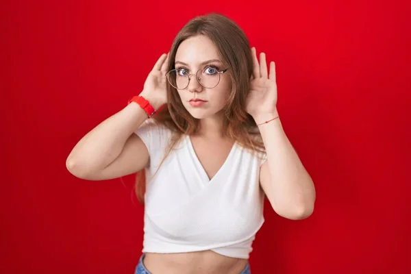 Ung Kaukasiska Kvinna Står Över Röd Bakgrund Försöker Höra Båda — Stockfoto