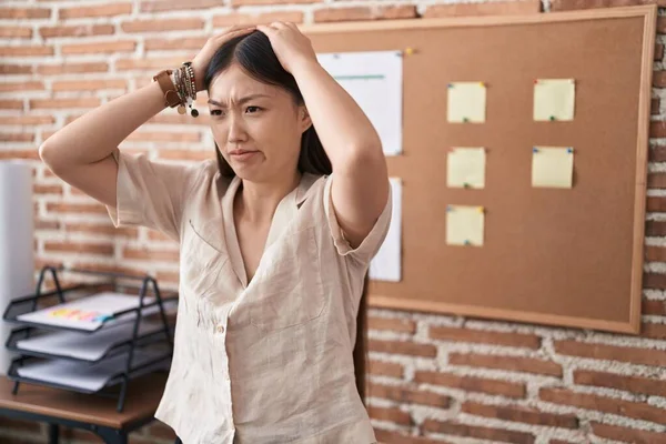 Chinese young woman working at the office doing presentation suffering from headache desperate and stressed because pain and migraine. hands on head.