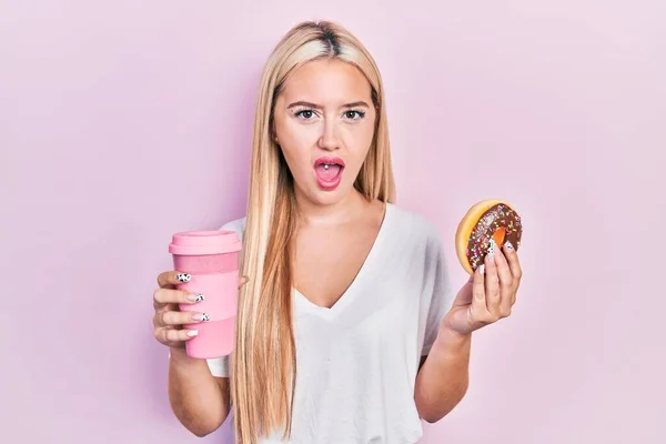 Chica Rubia Joven Comiendo Donut Tomando Café Cara Choque Mirando — Foto de Stock