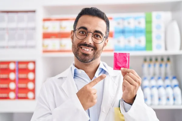 西班牙裔男子 留着胡子 手持避孕套 在药店工作 满脸笑容 手指手画脚 — 图库照片