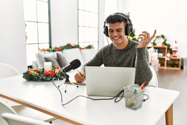 Young hispanic man radio worker working sitting by christmas tree at home