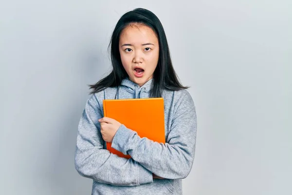 Young Chinese Girl Holding Book Shock Face Looking Skeptical Sarcastic — Photo
