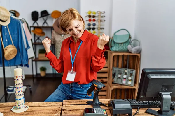 Middle age blonde woman working working as manager at retail boutique very happy and excited doing winner gesture with arms raised, smiling and screaming for success. celebration concept.