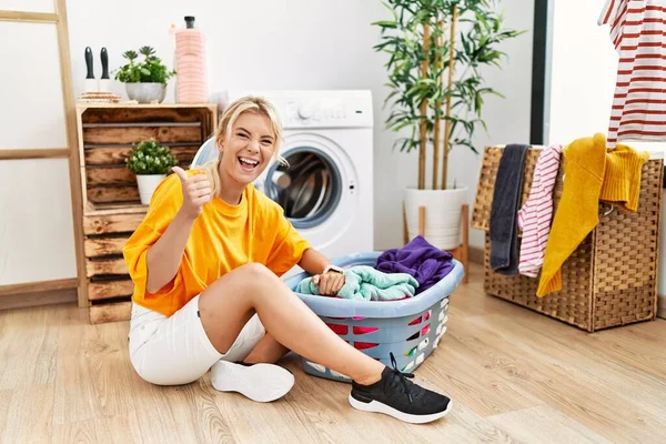 若い白人女性は手で積極的なジェスチャーを行うことを承認洗濯機に汚れた洗濯機を入れて 親指を笑顔と成功のために幸せ 勝者のジェスチャー — ストック写真