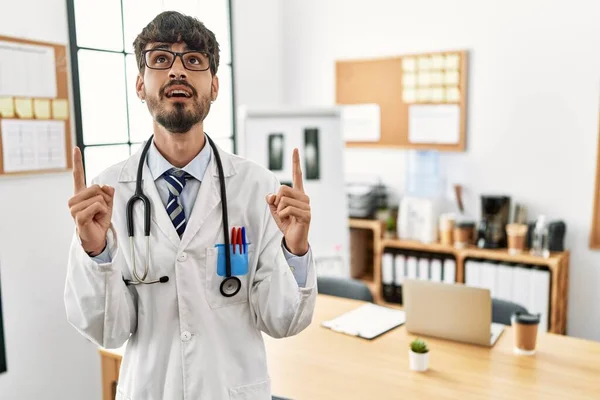 Hispanic Man Beard Wearing Doctor Uniform Stethoscope Office Amazed Surprised — Zdjęcie stockowe