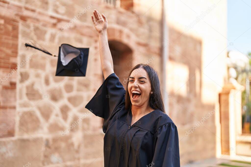 Young hispanic woman smiling confident throwing hat for graduation at university