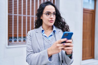 Genç İspanyol kadın yönetici caddede akıllı telefon kullanıyor.