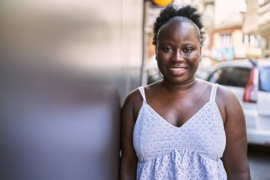 Genç Afrikalı Amerikalı kadın gülümseyerek şehirde mutlu mesut duruyor..