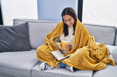 Genç İspanyol kadın kitap okuyor ve evde kahve içiyor.