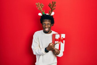 Geyik Noel şapkası takan Afrikalı genç bir adam endişeli, endişeli ve şaşırmış bir ifade takınıyor. 