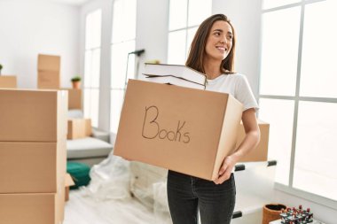 Genç İspanyol kadın gülümsüyor. Yeni evinde elinde kitap paketiyle kendinden emin.