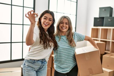 Mutlu bir şekilde gülümseyen genç çift yeni evin anahtarını ve karton kutuyu tutuyor..