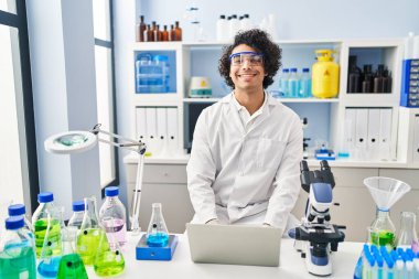 Laboratuvarda dizüstü bilgisayar kullanan Latin kökenli genç adam.