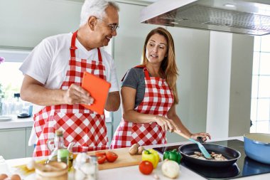Orta yaşlı İspanyol çift gülümsüyor. Mutfakta yemek pişiriyor ve dokunmatik ped kullanıyor..